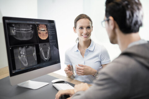 Röntgenaufnahme auf dem PC und eine Assistenzärztin unterhält sich gerade mit dem Patienten über das Ergebnis